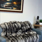 Living room with a gray sofa covered by a fur throw, a painting on the wall, and a logo in the corner.