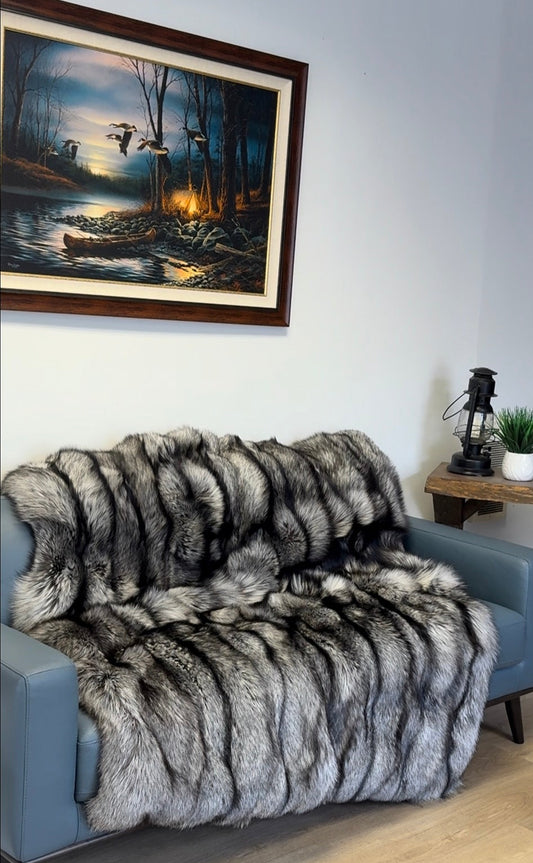 Living room with a gray sofa covered by a fur throw, a painting on the wall, and a logo in the corner.